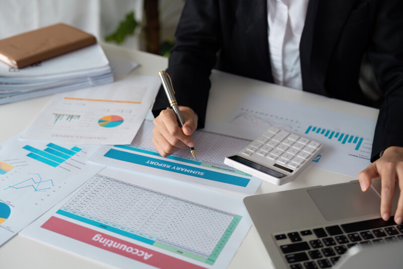 Business professional analyzing financial reports with a laptop, calculator, and charts in an office setting.